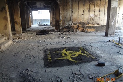 تركيب أرضية لعلامة خطر بيولوجي في الطابق الثاني من مبنى شديد السمّية تعرض للتفجير في بغداد عام 2016. تم تنفيذ العمل بصبغة خاصة (مسحوق مادة)، 2016 ، بغداد.