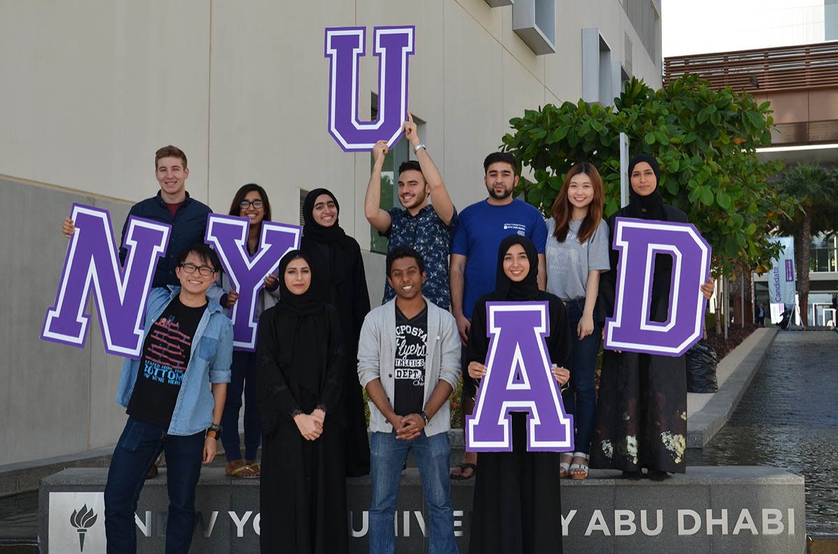 Students posing with a NYUAD sign on campus. 