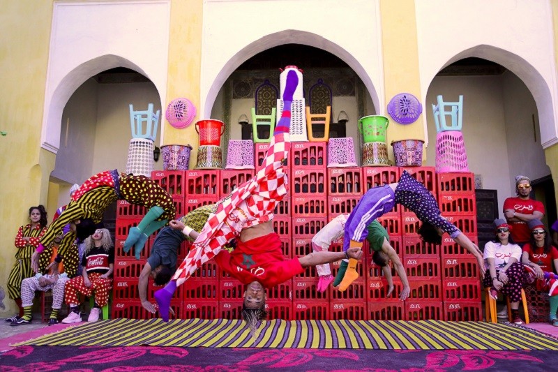 The group performs acrobatics in colorful costumes, flipping and jumping through the air.