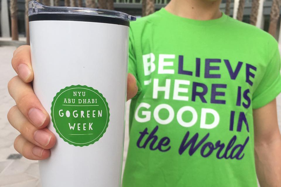 A student holding the NYUAD Go Green Week mug and dons a green shirt.