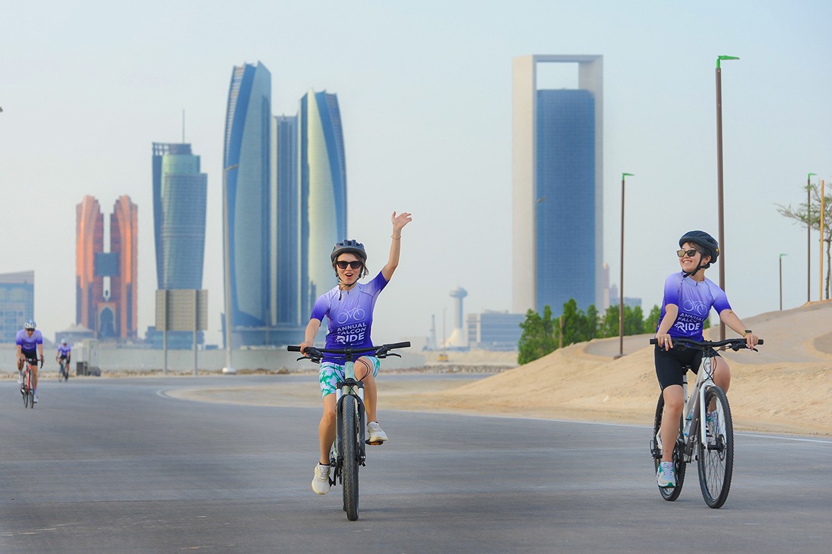 Two riders in the foreground, one waves to the camera. The skyline and a few other riders are in the background.