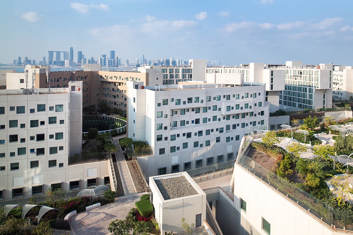 An aerial view of the NYUAD Saadiyat Island campus, with buildings, the High Line in view, and the Abu Dhabi skyline in the background.