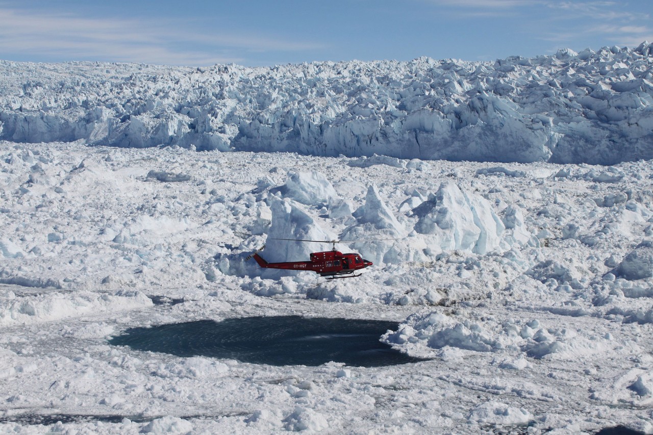 Investigation of properties of the mélange and underlying waters in front of the calving front at Jakobshavn Glacier in west Greenland via airborne probes from a hovering helicopter. Glacier calving front cliff seen in background, mélange in foreground with helicopter.