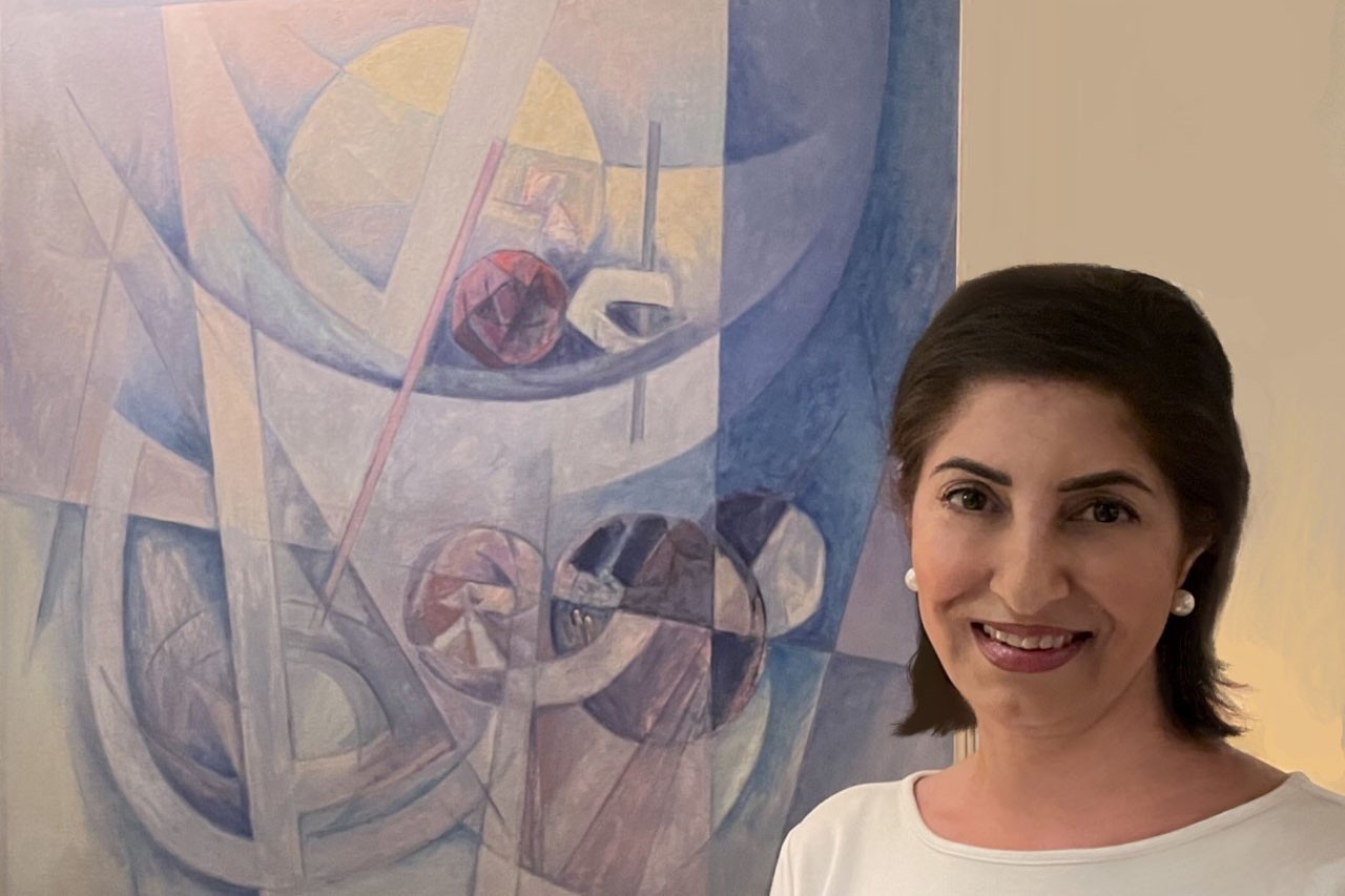 Lubna Hammad standign next to a painting by her father, and painter, Mahmoud Hammad