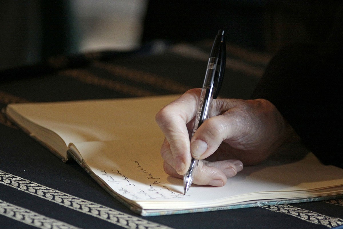 A person writing in a note book with a pen.