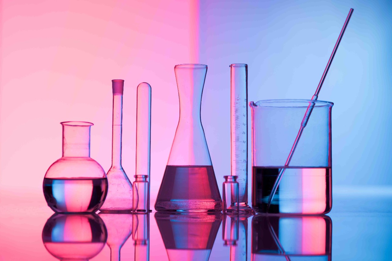 Different laboratory glassware with water and empty with reflection. Pink and blue tint background