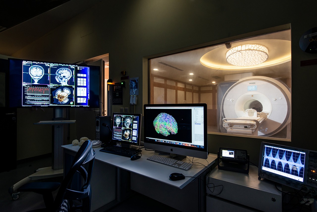 A view of an MRI lab with brain scans on several monitors and an MRI scanner in the background.